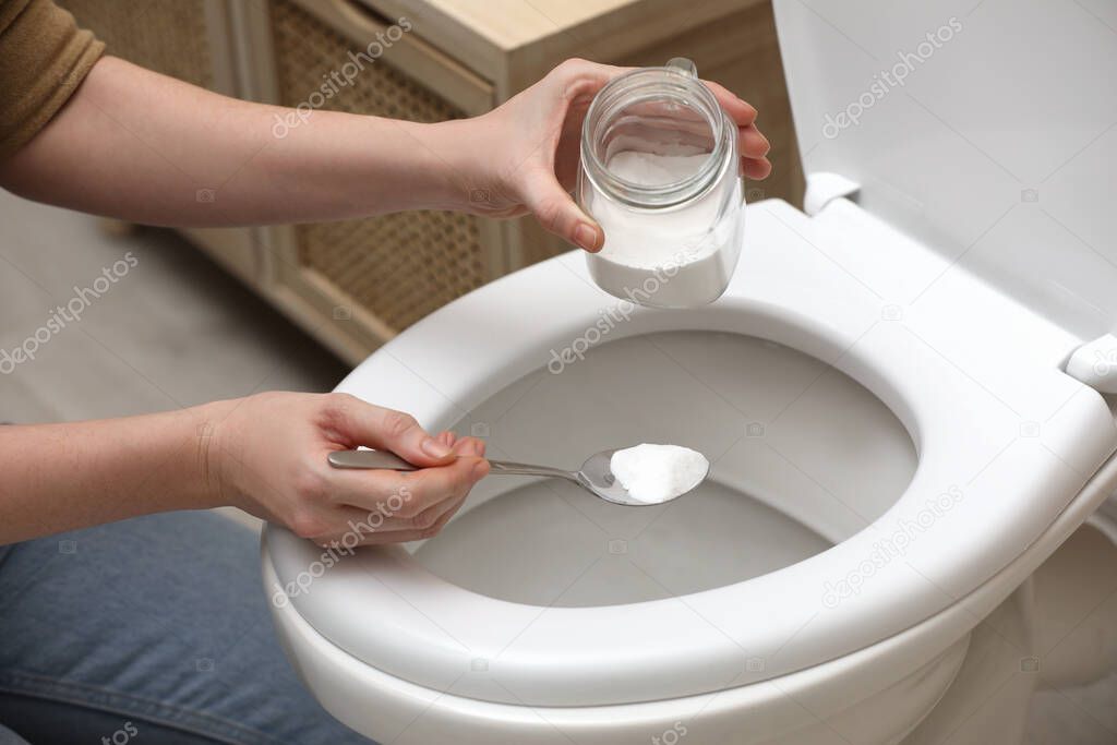 Woman cleaning toilet bowl with baking soda, indoors closeup