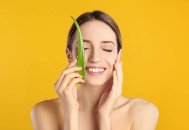 Sarı arka planda aloe yaprağı olan mutlu genç bir kadın.