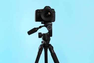 Açık mavi arka planda profesyonel kamerası olan modern tripod.