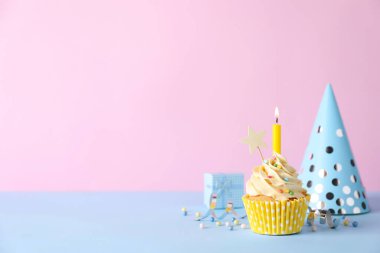 Doğum günü pastası yanan mum, parti dekorasyonu ve hediye paketi açık mavi masada pembe arka planda, mesaj için boşluk
