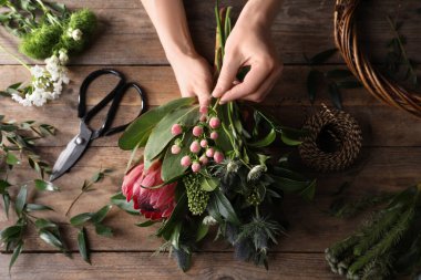 Çiçekçi, ahşap masada taze çiçeklerle güzel bir buket yapıyor.