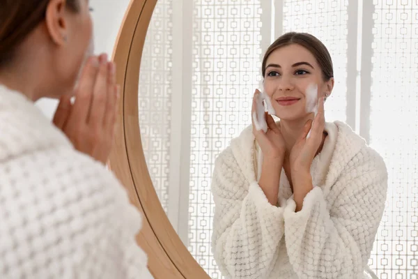 Ung Kvinna Applicera Rengöringsskum Hennes Ansikte Nära Spegeln Badrummet — Stockfoto