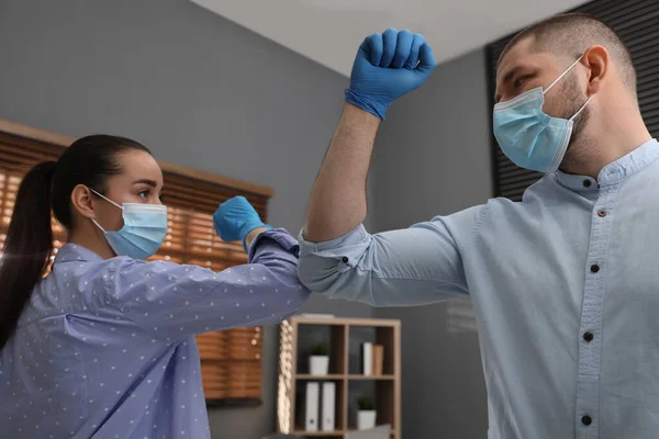 Office employees in masks greeting each other by bumping elbows at workplace