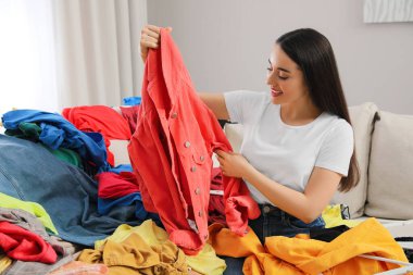 Odadaki kanepede bir sürü elbisesi olan mutlu genç bir kadın. Hızlı moda.