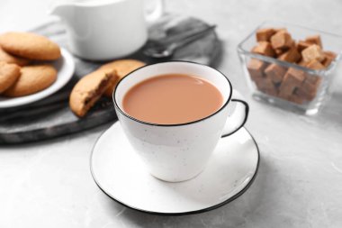 Gri masadaki kurabiyelerin yanında beyaz bardakta sütlü lezzetli çay.