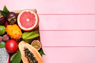 Pembe ahşap arka planda, kutuda farklı tropikal meyveler var. Metin için boşluk