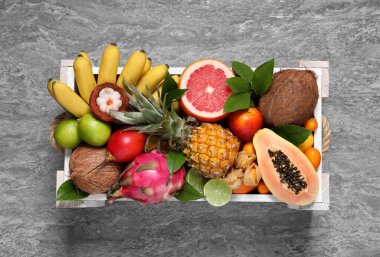 Gri arka planda, ahşap kutuda farklı tropikal meyveler.