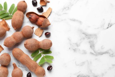 Olgun tamarindler ve beyaz mermer masa üzerinde taze yapraklar, düz. Metin için boşluk