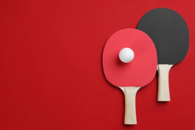 Ping pong raketleri ve top kırmızı arka planda, düz yerde. Metin için boşluk