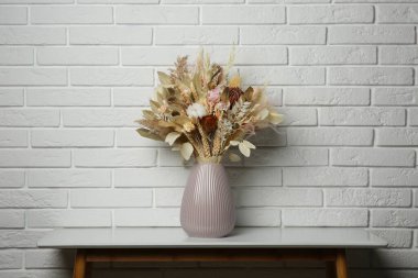 Beyaz tuğla duvarın yanındaki masada seramik vazoda kurutulmuş güzel çiçek buketi.