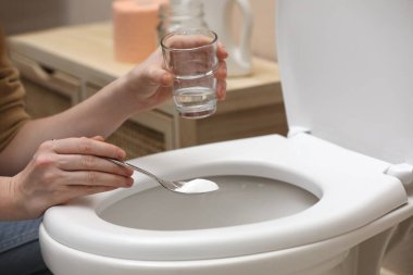 Kadın tuvalet kabını kabartma tozuyla temizliyor. Kapalı mekanda.