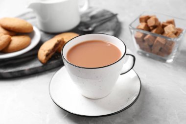 Gri masadaki kurabiyelerin yanında beyaz bardakta sütlü lezzetli çay.