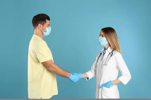 Medico Paziente Maschere Protettive Stringendo Mani Sfondo Azzurro — Foto Stock