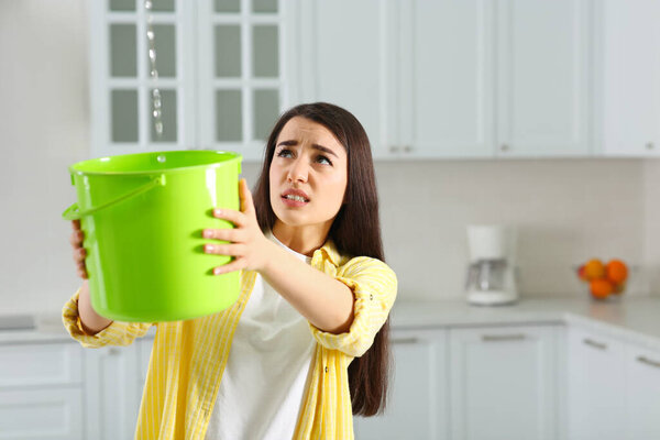 Молодая женщина собирает протекающую воду с потолка на кухне, место для текста. Время вызова службы ремонта крыш