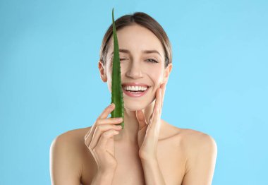 Açık mavi arka planda aloe yaprağı olan mutlu genç bir kadın.