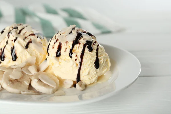 Delicious banana ice cream with toppings on white wooden table, closeup