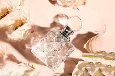 Bir şişe aromatik parfüm ve bej arka planda çiçekler.