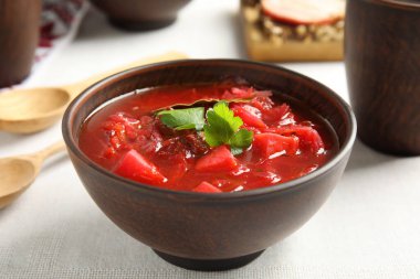 Ukrayna borsch 'u beyaz masa örtüsünde servis edilen şık kahverengi kil kase, yakın plan.