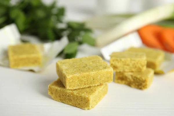 Bouillon cubes and other ingredients for soup on white wooden table, closeup