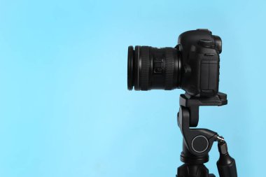 Açık mavi arka planda profesyonel kamerası olan modern tripodlar. Metin için boşluk