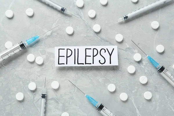 Sheet of paper with word Epilepsy, pills and syringes on grey marble table, flat lay