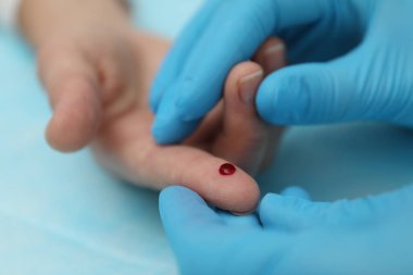 Doktor masadaki hastanın parmağından kan örneği alıyor.