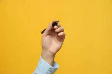 Sarı arka planda elinde kalem tutan solak kadın, yakın plan.