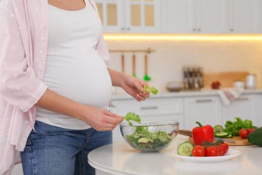 Genç hamile kadın mutfakta sebze salatası hazırlıyor, yakın plan. Sağlıklı beslenme