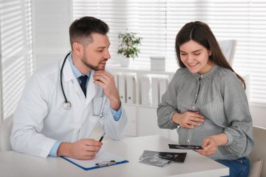 Klinikteki doktor randevusunda ultrason fotoğrafı olan hamile bir kadın.