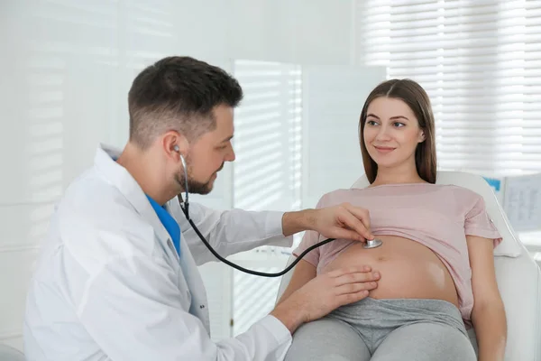 Doctor examining pregnant woman with stethoscope in clinic