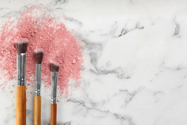 Makeup brushes and scattered eye shadow on white marble table, flat lay. Space for text