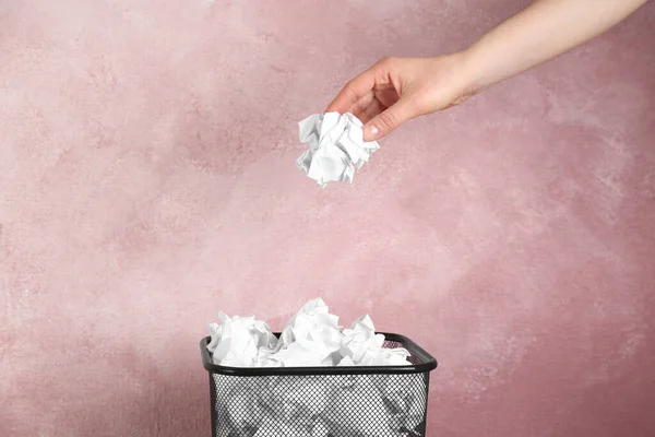 Woman throwing crumpled paper ball into basket on pink background, closeup