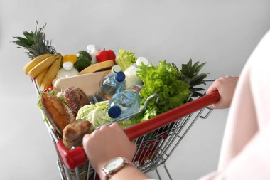 Gri arka planda alışveriş arabası dolu bir kadın, yakın plan.