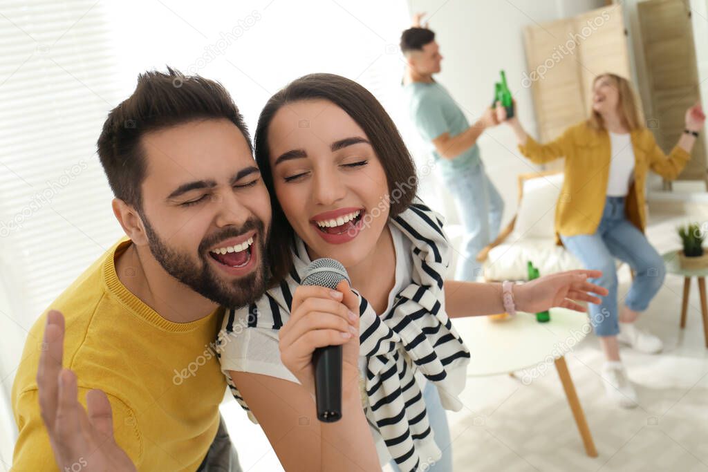 Happy couple singing karaoke with friends at home