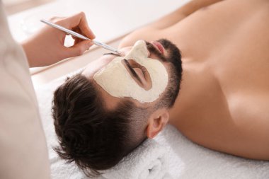 Kozmetik uzmanı spa salonunda adamın yüzüne maske takıyor.
