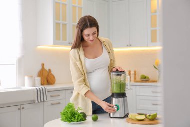 Genç hamile kadın mutfaktaki masada smoothie hazırlıyor. Sağlıklı beslenme