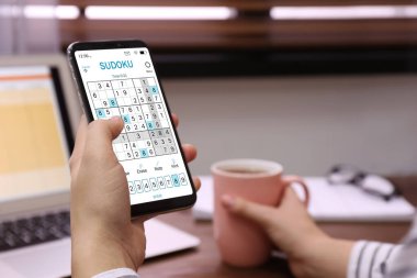 Akıllı telefondan sudoku oyunu oynayan kadın kapalı alanda, yakın plan.