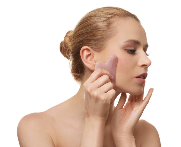 Красивая молодая женщина делает массаж лица с помощью гуа ша инструмент на белом фоне