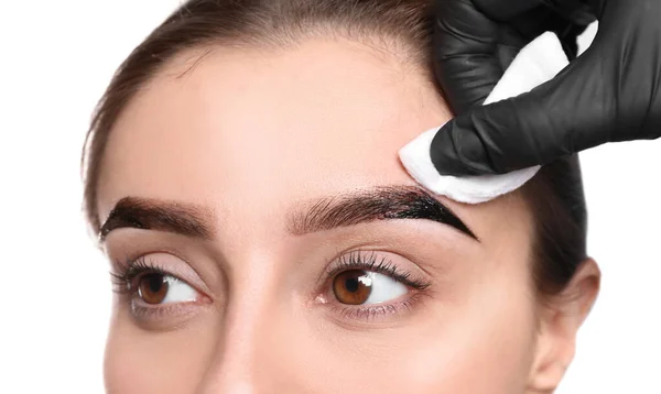 Beautician wiping tint from woman\'s eyebrows on white background, closeup