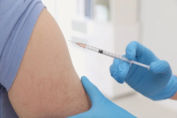 Doctor giving injection to man in hospital, closeup. Immunization concept