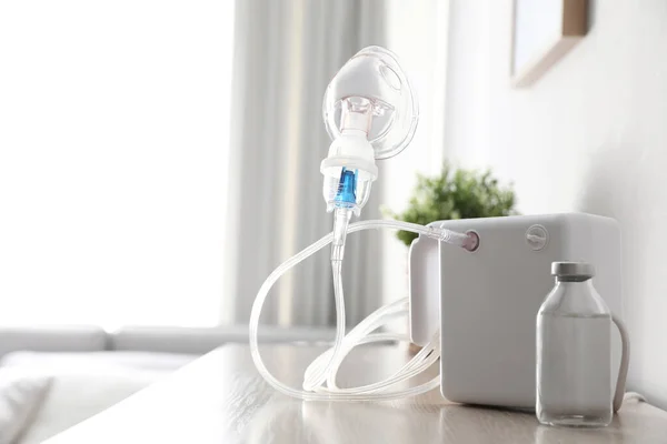 Modern nebulizer with face mask and liquid medicine on wooden table indoors. Inhalation equipment