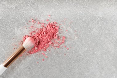 Gri taş arka planda makyaj fırçası ve dağınık göz farı, üst manzara. Metin için boşluk