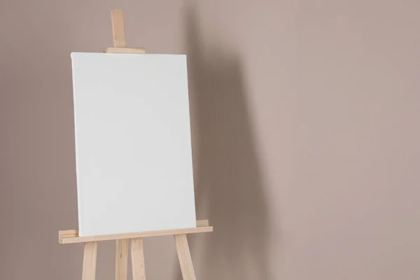 Wooden easel with blank canvas on beige background. Space for text