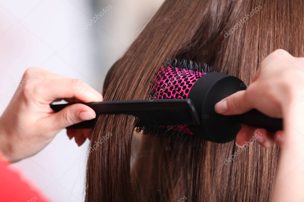 Stylist brushing woman's hair in salon, closeup