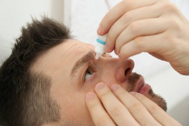 Kapalı alanda göz damlası kullanan adam, yakın çekim görüntüsü