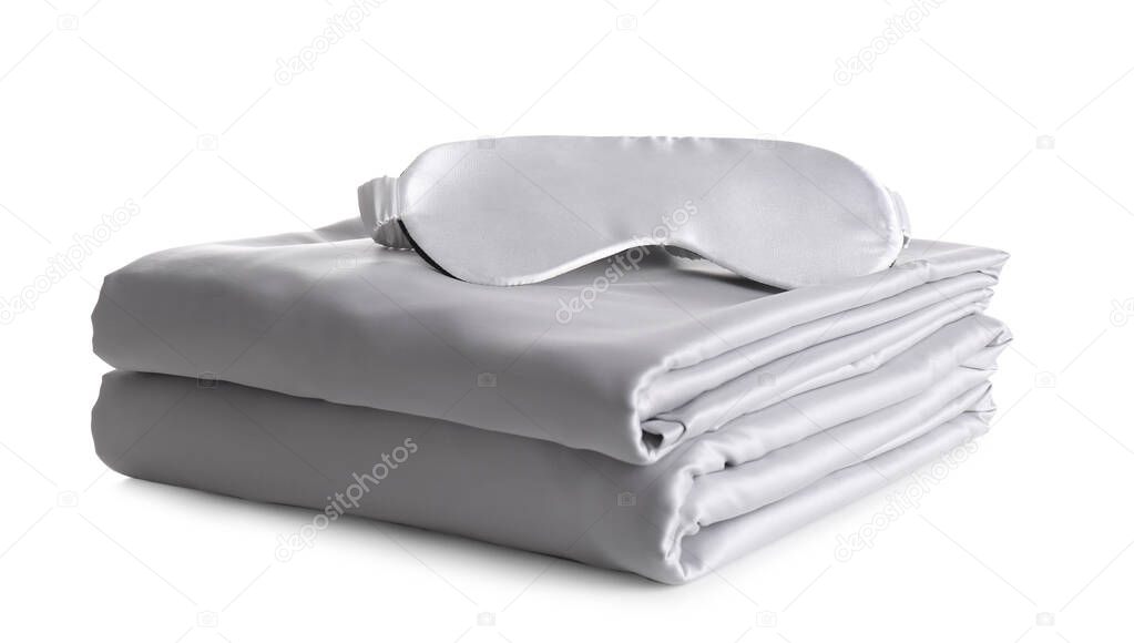 Stack of clean silky bed linen and sleeping mask isolated on white