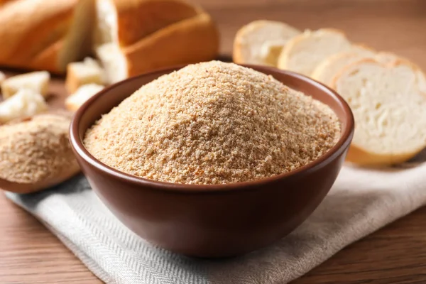 Fresh bread crumbs in bowl on wooden table, closeup