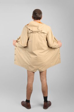 Exhibitionist exposing naked body under coat on light background, back view clipart