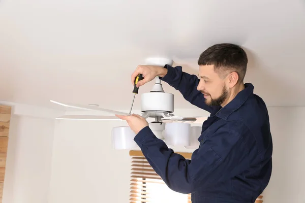 Electrician with screwdriver repairing ceiling fan indoors