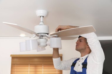 Elektrikçi tavan vantilatörünü içeride lambayla onarıyor.